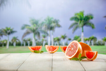 Grapefruit halves with mint leaves on white wooden  table top with palm trees background. Summer sunlight. Copy space for food and drinks and products.