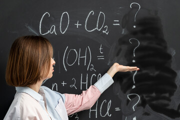 Confused female student writing the formula of a chemical reaction on the blackboard	