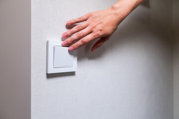Close-up of a woman's fingers and hand on the light switch at home. Power and energy, energy saving