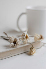 Book, white dried flowers and mug with coffee