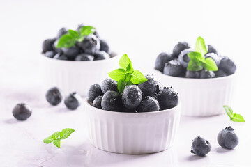 Tasty aromatic blueberries with waterdrops in white ceramic bowls on light marble background close up.