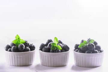 Tasty aromatic blueberries in white ceramic bowls on light marble background close up.

