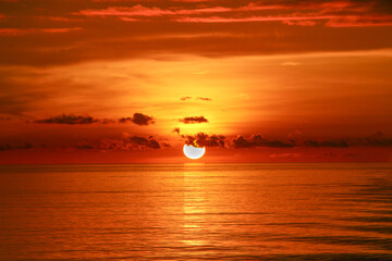 Bright red sun setting down at the horizon over the ocean