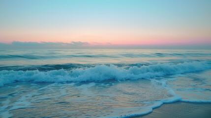 Obraz premium Gentle waves roll onto the sandy shore at sunset, with a pink and blue sky reflected on the water, creating a calm and peaceful beach scene.