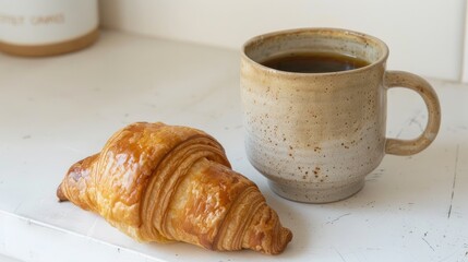 Croissant next to artisan coffee mug on a white backdrop