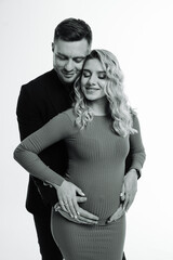 Pregnant Couple Posing for Portrait. A black and white portrait of a pregnant woman and her partner, both looking lovingly at her belly.