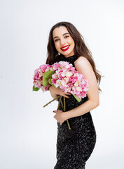 Woman Holding Pink Flowers in Black Dress. A woman in a black sequined dress smiles and holds a bouquet of pink hydrangeas.