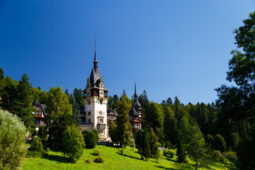 The Peles castle surrounded by splendid parklands in the town of Sinaia, Transylvania, Carpathian Mountains, Romania, Summer time, bright sunny day with dark blue sky