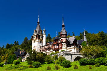 The Peles castle surrounded by splendid parklands in the town of Sinaia, Transylvania, Carpathian Mountains, Romania, Summer time, bright sunny day with dark blue sky