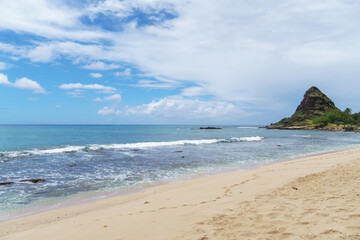 Beach with mountain, ocean waves, cloudy sky in background