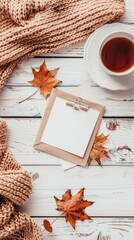 Cozy home desk table with knitted plaid, tea cup, fall leaves, letter with blank paper card on wooden white background. Top view, flat lay, copy space. Autumn composition. Nordic hygge style concept 