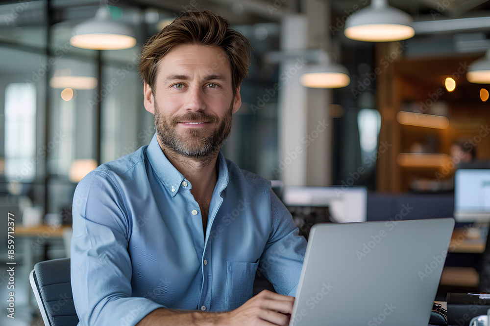 Wall mural portrait of a successful and confident young man in a blue shirt sitting in the office at a desk, wo