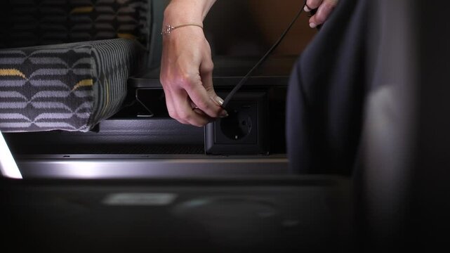 a girl passenger in a modern train carriage connects a USB cable to a socket