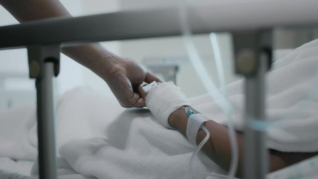 Close up shot of mother holding hand of sick daughter while lying down on bed in the hospital