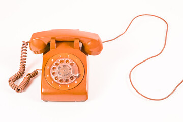 Vintage orange rotary dial telephone with a coiled cord, on a white background, studio shot.