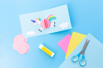 Pair of scissors atop paper in child's craft featuring a unicorn card template with a blue theme. Ideal for creative projects and educational concepts