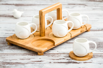 Small plain porcelain coffee cups on bamboo tray on white wooden table.