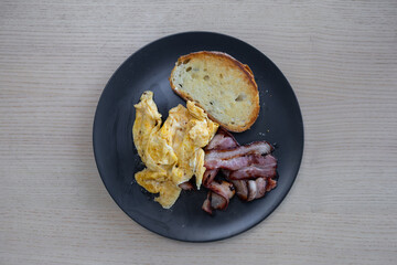A breakfast plate of scrambled eggs, bacon, and bread.
