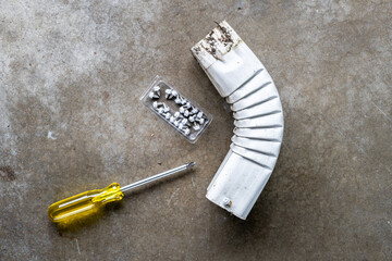 Phillips head screwdriver and box of new metal gutter screws and a corner section of rectangular...