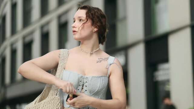 Pretty young caucasian woman stopped to check makeup and putting pomade lipstick for lips at city centre Charming female preparing for new day and smiling to mirror outdoors