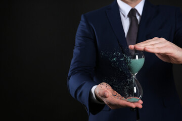 Businessman holding dissolving hourglass on black background, closeup. Time is running out
