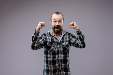 Bearded man with clenched fists celebrating success on grey back