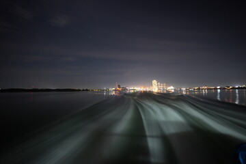 船から遠くの街を眺める 夜の海越しに見える街の光、光の反射