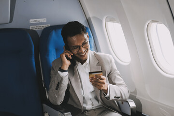 Businessman holding credit card and looking at camera near laptop in private jet