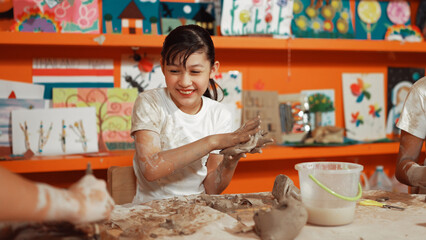 Asian highschool student modeling clay on table with mud and bottle of water at pottery workshop. Group of happy diverse children working or making cup of clay. Creative activity concept. Edification.