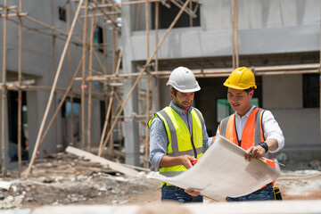 Asian male civil engineer and caucasian male architect wears safety vest with helmet discuss and...