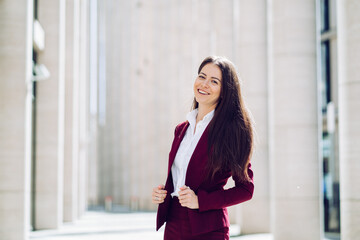 Fototapeta premium confident businesswoman in a burgundy suit standing and smiling in a modern urban setting