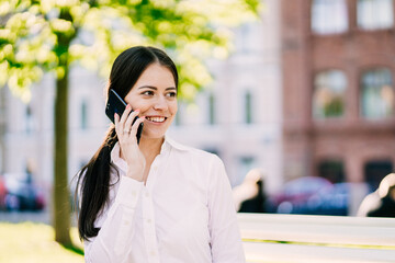 smiling woman in a white shirt talking on the phone in an outdoor urban setting