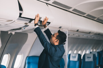 man putting luggage on the top shelf on airplane