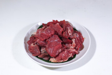 fresh beef cut into cubes and served on a white plate with a banana leaf cover and photographed from the front