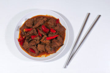 beef cooked in rendang with a garnish of cayenne pepper, served on a plate and aluminum chopsticks beside it