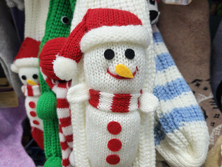 There are knitted white mittens with a snowman hanging in the store. The concept of Christmas and New Year.