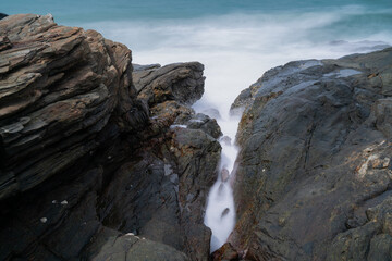 The waves crash against the rocks on the shore