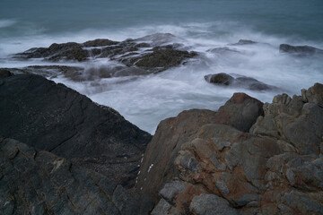 The waves crash against the rocks on the shore