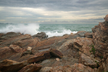 Waves crashing against the orange rocky shore in the evening