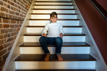 Barefoot boy in blue jeans and white sweater leaning back casually sitting on stairs