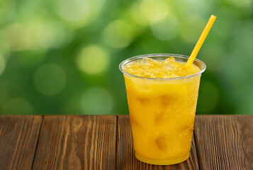 disposable plastic glass of cold orange juice with ice and straw