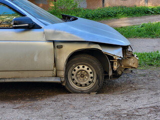 A gray wrecked car parked on the side of a city road