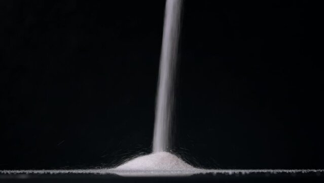 Pile of sugar. Stream of sugar falls from above on black background. 