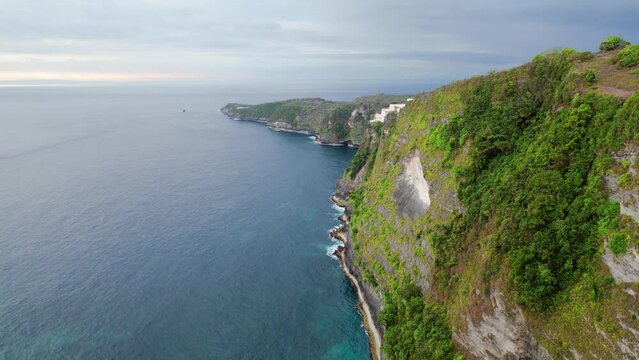 aerial drone shot panning showing the beautiful coast sea with green hills in hte Nusa Penida area in Kellingking showing the tropical paradise in bali Indonesia