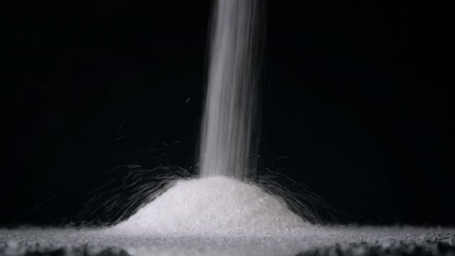 Close up of a pile of sugar. Stream of sugar falls from above on black background. 