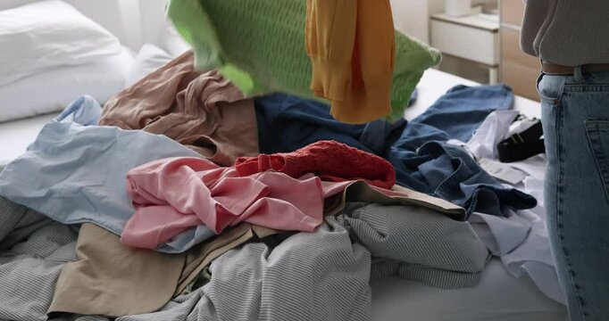 Woman not knowing what clothes to choose. Pile of Clothes on Bed.  messy bed with many products on it. Consumer culture of buying too many. coming home after shopping. buying too much