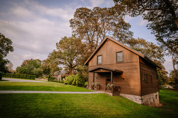 Blome, Latvia - September 11, 2023 - Rustic wooden house surrounded by lush green lawn, trees, and a stone pathway under a partly cloudy sky, creating a serene countryside scene. Copy space.