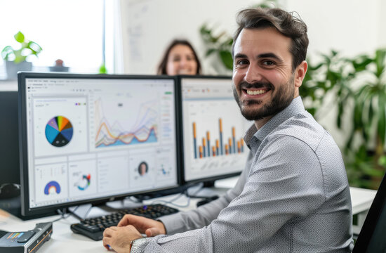 A happy professional man with beard wearing glasses and suit sitting at his desk in front of the computer, on screen is showing data visualization charts