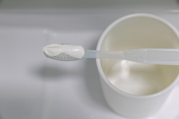 Toothpaste on toothbrush resting on top of white cup in clean bathroom, dental hygiene and healthy habits and lifestyle concept