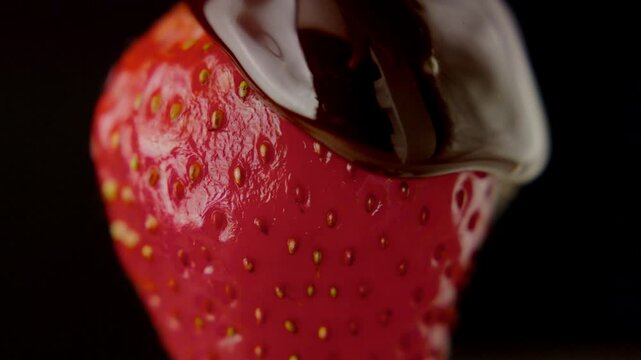 Closeup footage of the melted chocolate syrup covering a strawberry, isolated on a black backgorund